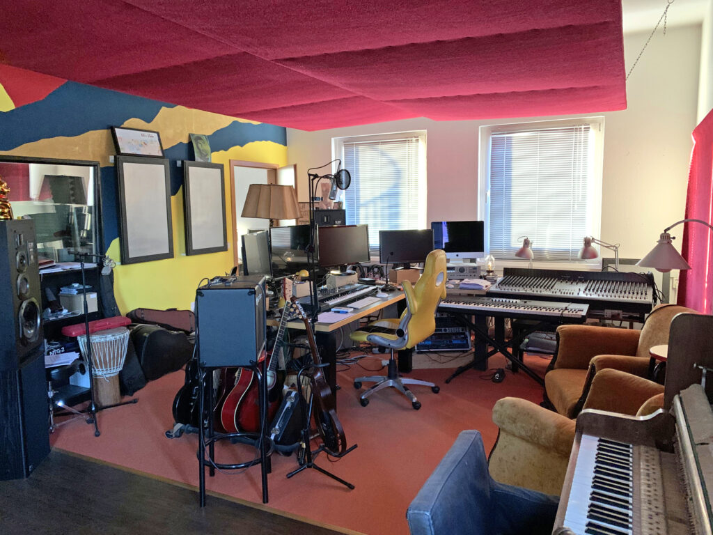 Ein Blick ins Studio der Hörspielfabrik. Man sieht einen Schreibtisch, Stühle, ein Klavier und ein Mischpult.